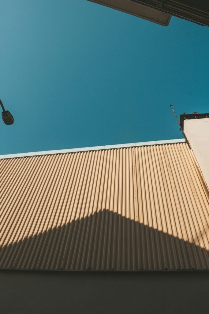 Explore architectural design with geometric shadows on a corrugated roof under a clear blue sky.