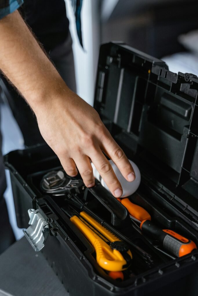 Close-up of a hand reaching into a toolbox with assorted tools inside, indoors.